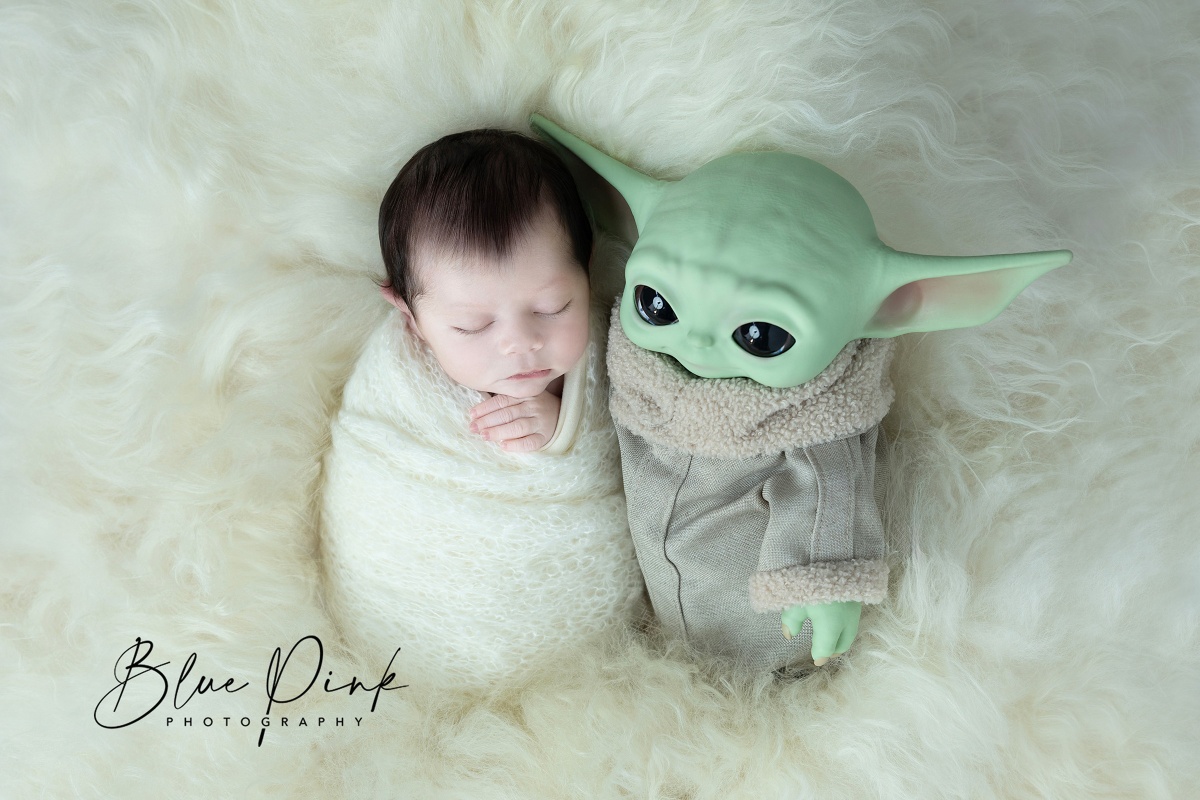 Adorable newborn baby peacefully wrapped in a soft knitted white blanket, nestled next to a charming Yoda toy.